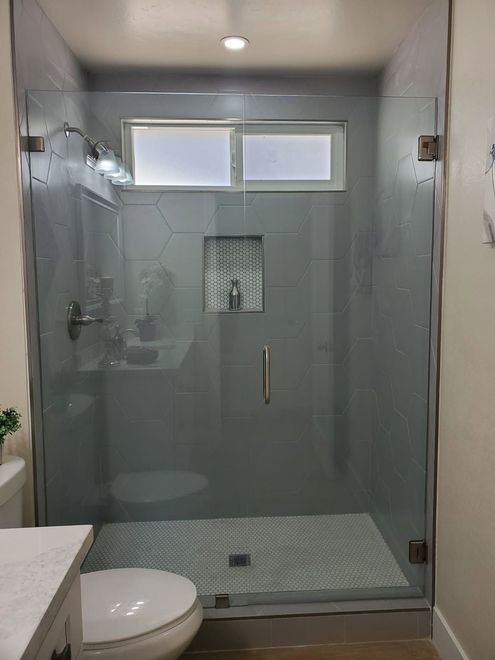A walk-in shower with gray hexagonal wall tiles, a mosaic tile floor, glass door, and a built-in recessed shelf.