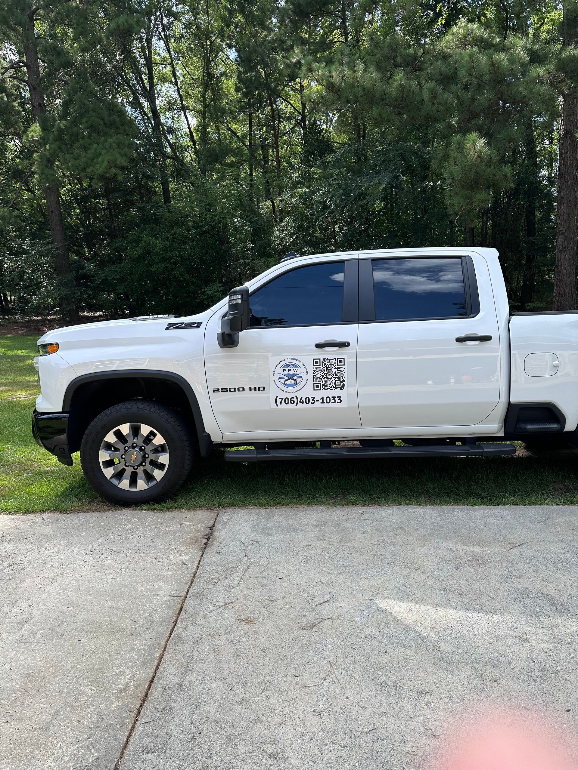 White pickup truck parked on concrete, with company logo and forested background.