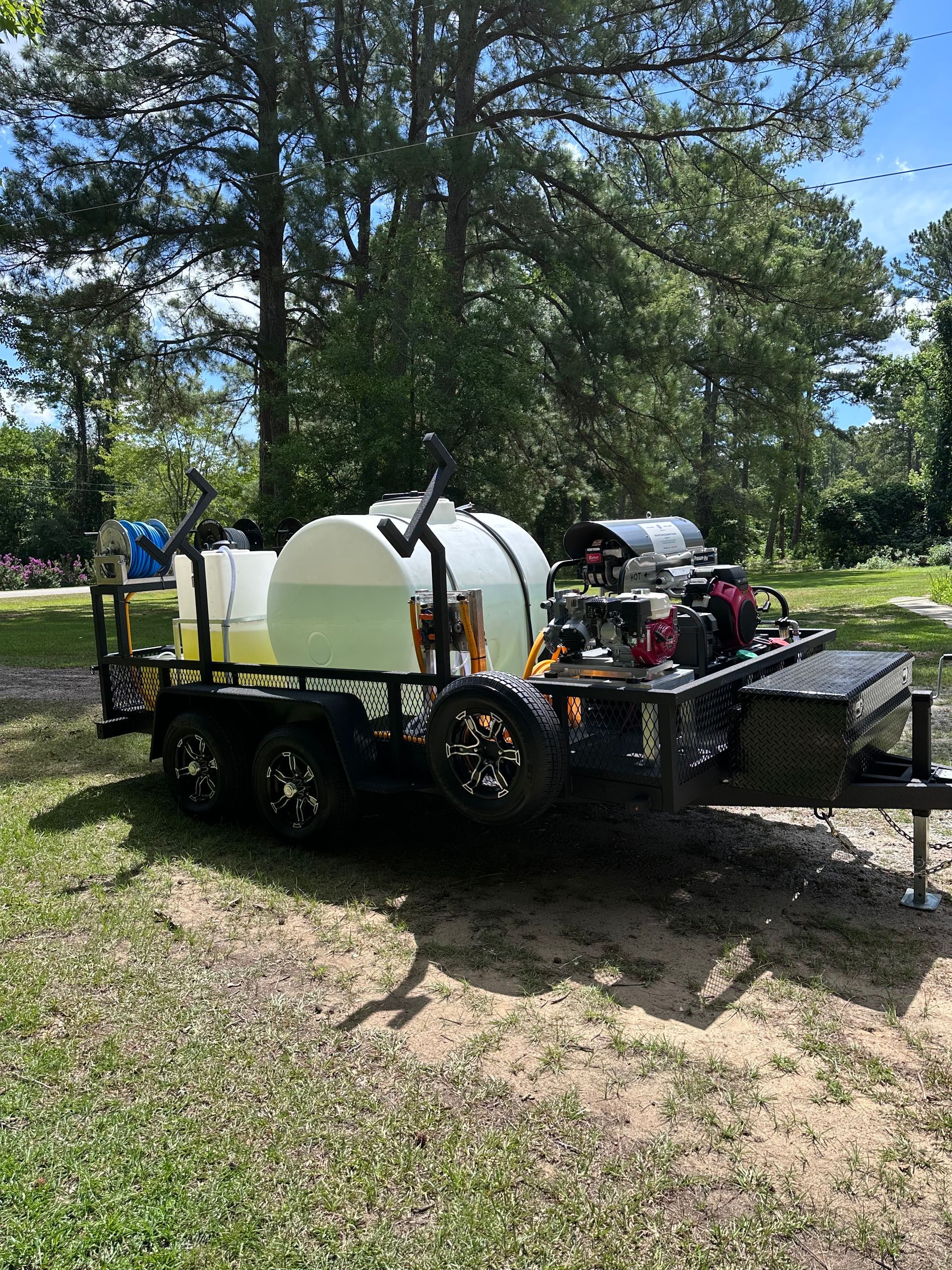 A trailer with two white water tanks and a pressure washer. Green liquid visible, parked on grass.