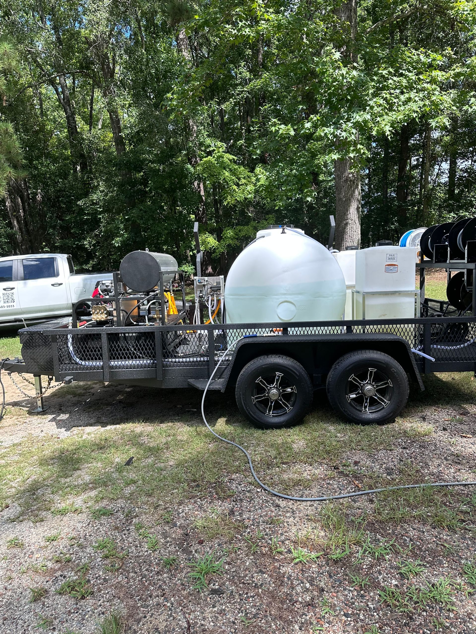 A utility trailer with a water tank, hoses, and equipment, parked on grass.