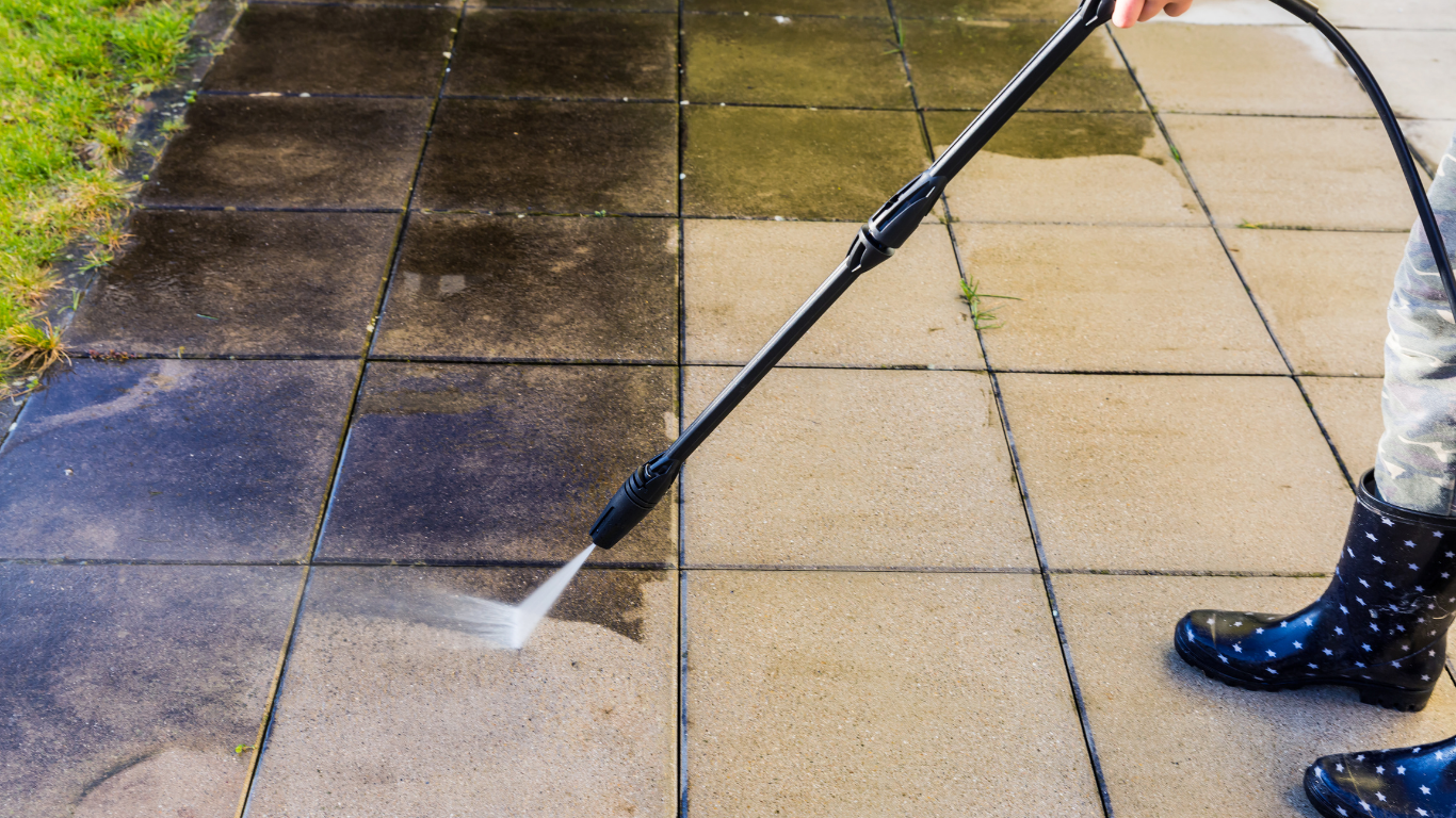 Pressure washer cleaning a dirty patio, revealing the cleaned, lighter stone.