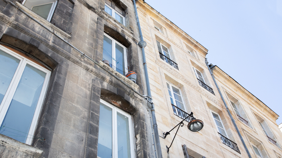 Half of a building façade cleaned; revealing a bright, stone color next to the darkened, dirty section.