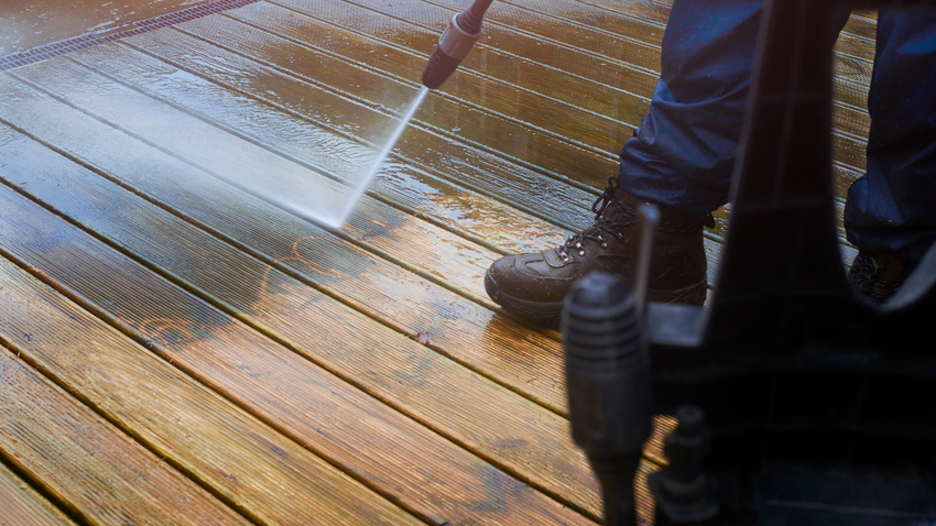 Person in boots power washing a wooden deck.