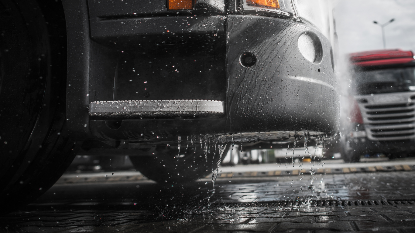 Semi-truck being washed; water dripping from step and front bumper.