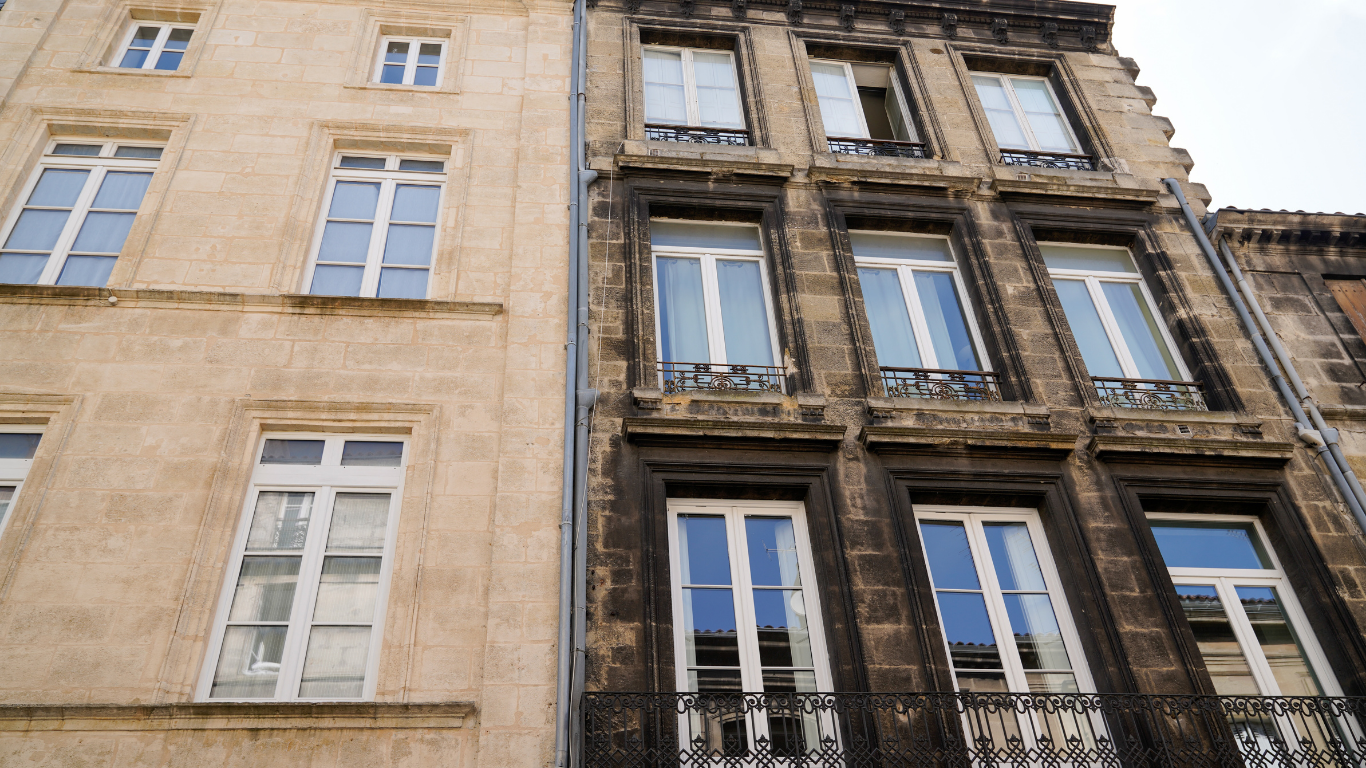 Two adjacent buildings, one cleaned beige, the other dark and dirty.