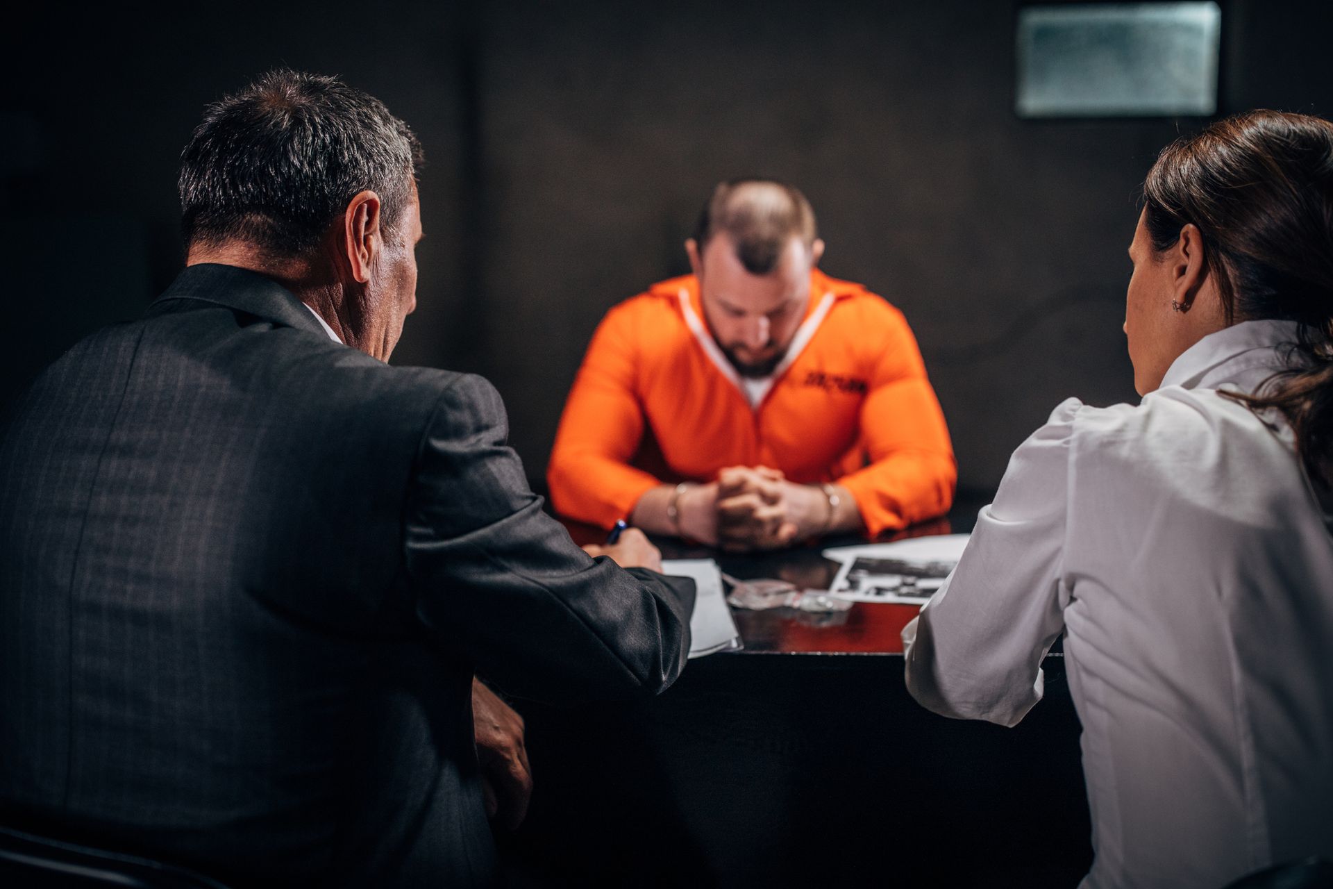 Man with handcuffs and two criminal defense attorneys sitting in the investigation room.