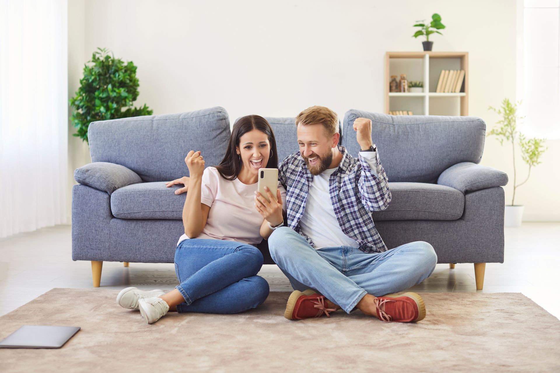 A man and a woman are sitting on the floor in front of a couch looking at a cell phone.