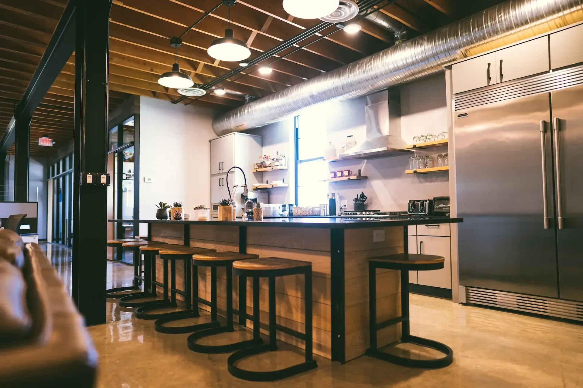 A kitchen with a long counter and stools and a refrigerator.