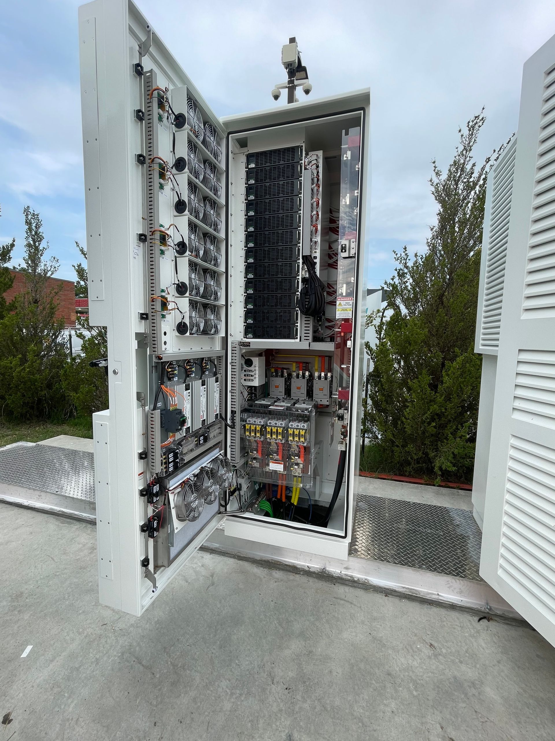 Open electrical control cabinet with wiring and components outdoors on a concrete pad