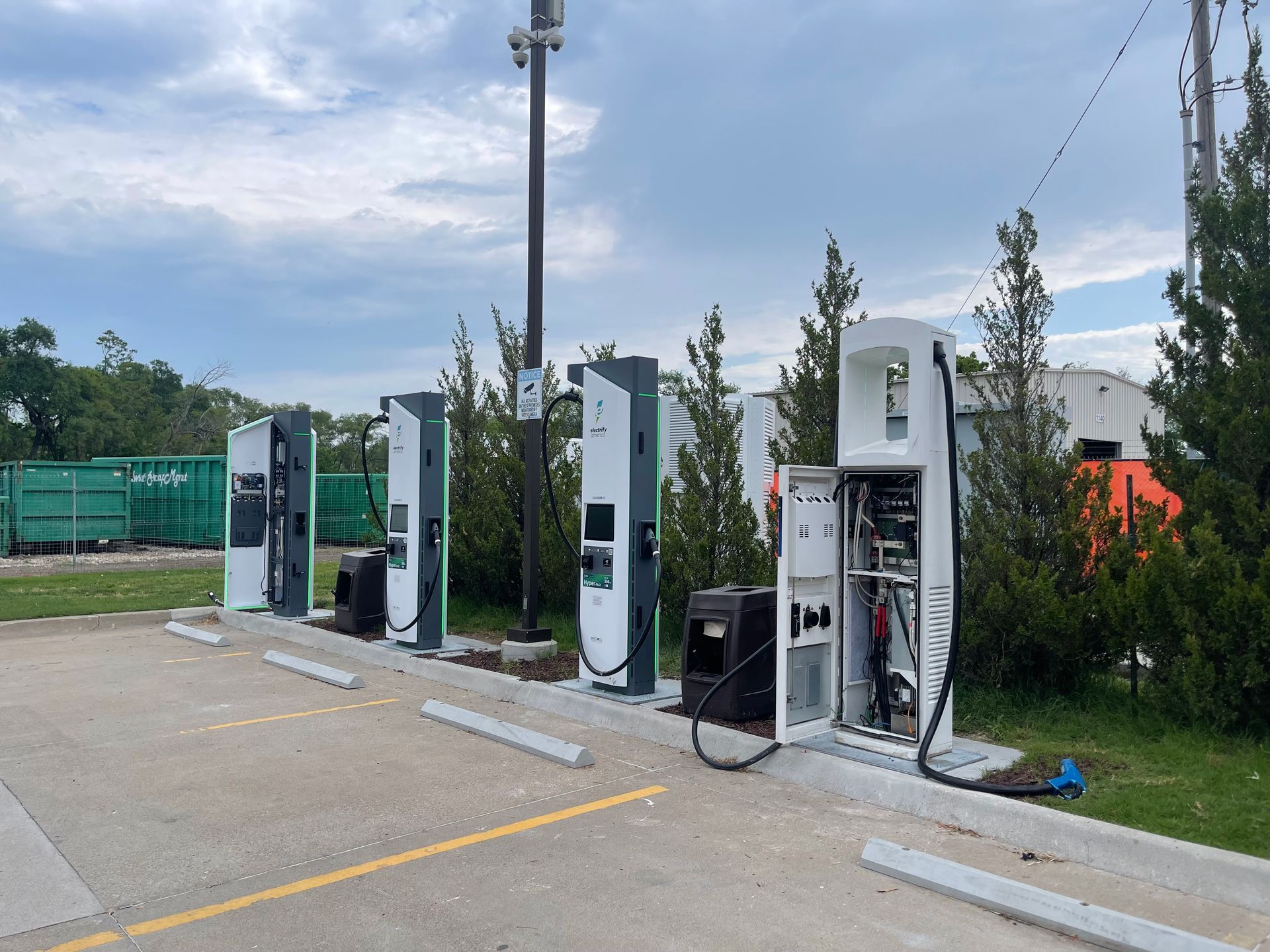 Outdoor row of electric vehicle charging stations beside a parking lot and greenery
