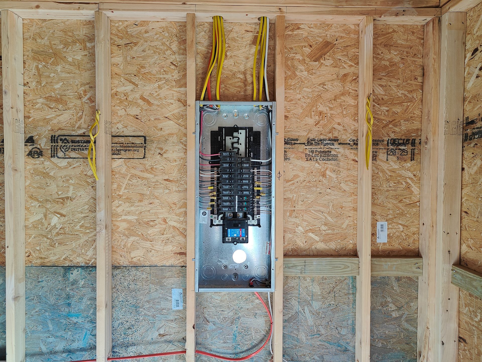 Electrical panel mounted in a framed wall with exposed wiring and insulation