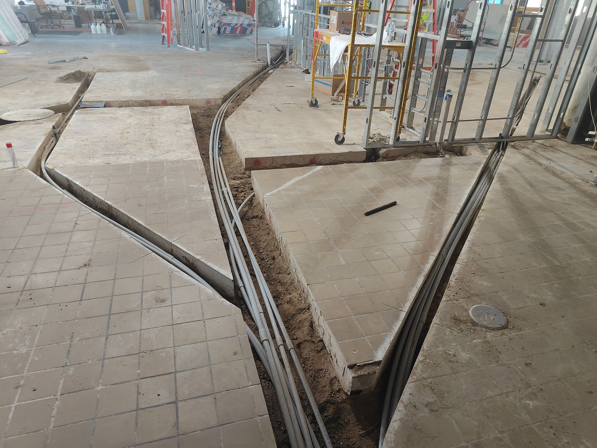 Construction site with open trench cuts in tiled floor and concrete pavement
