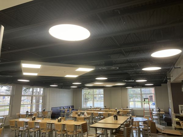 Bright classroom with wooden tables and chairs under circular ceiling lights and large windows