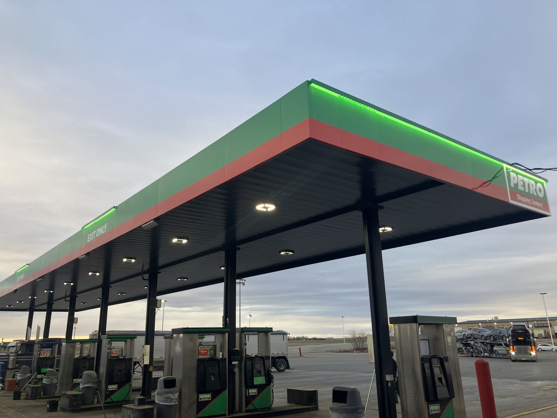 Gas station canopy with green and red trim over fuel pumps at dusk