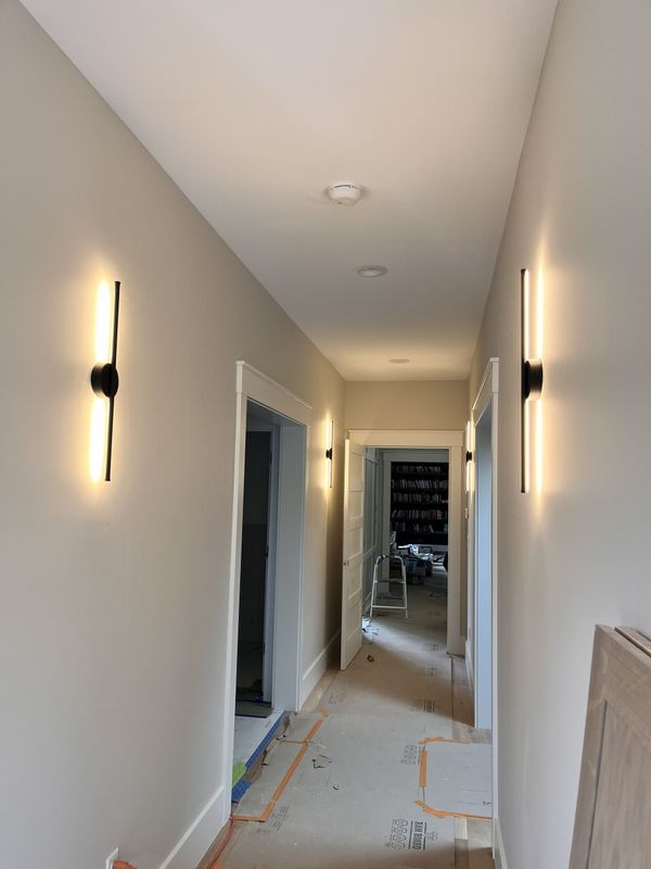 Narrow hallway under renovation with wall sconces, white walls, and floor protection covering the floor