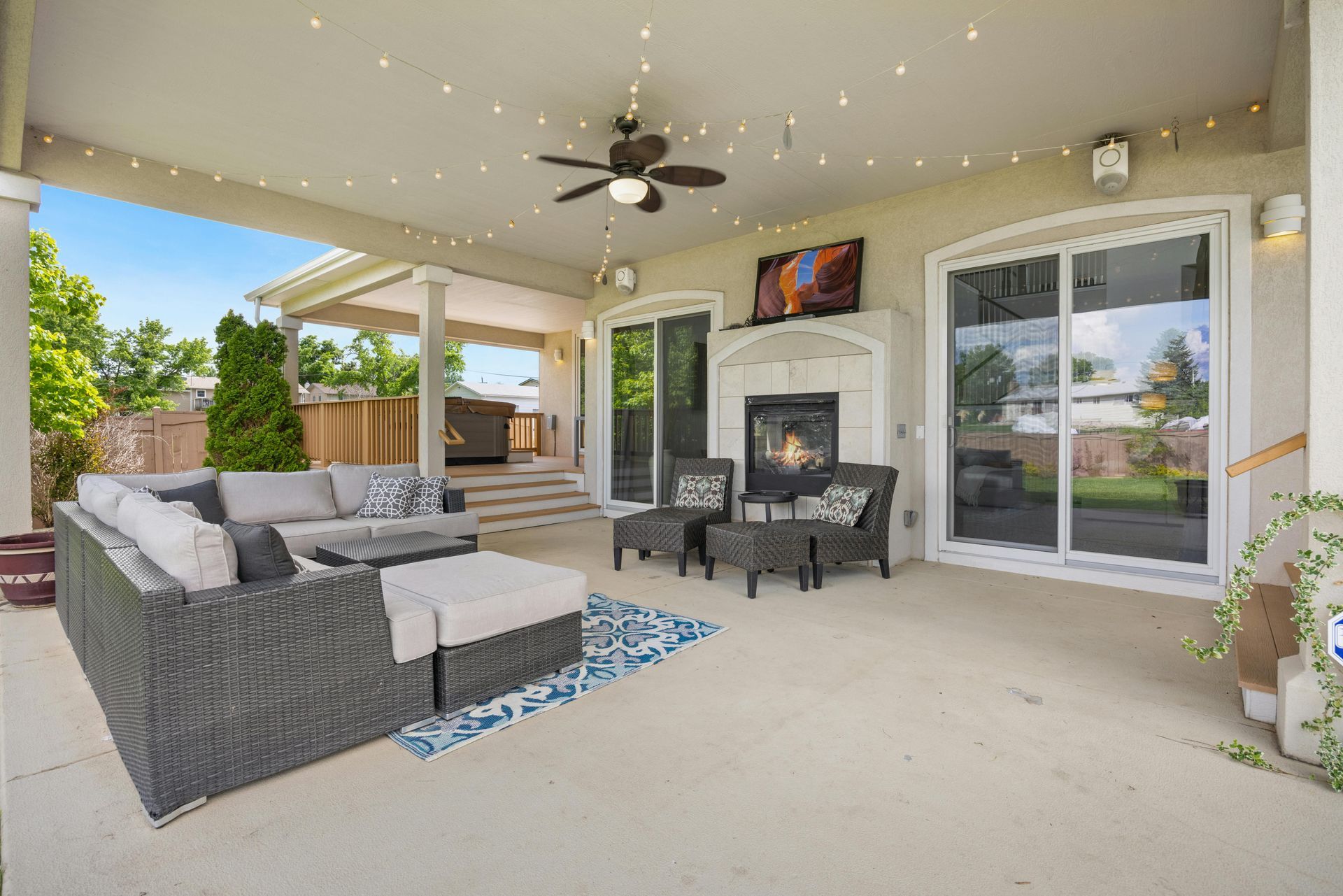 Covered patio with wicker sectional, fireplace, ceiling fan, and sliding glass doors opening to a backyard