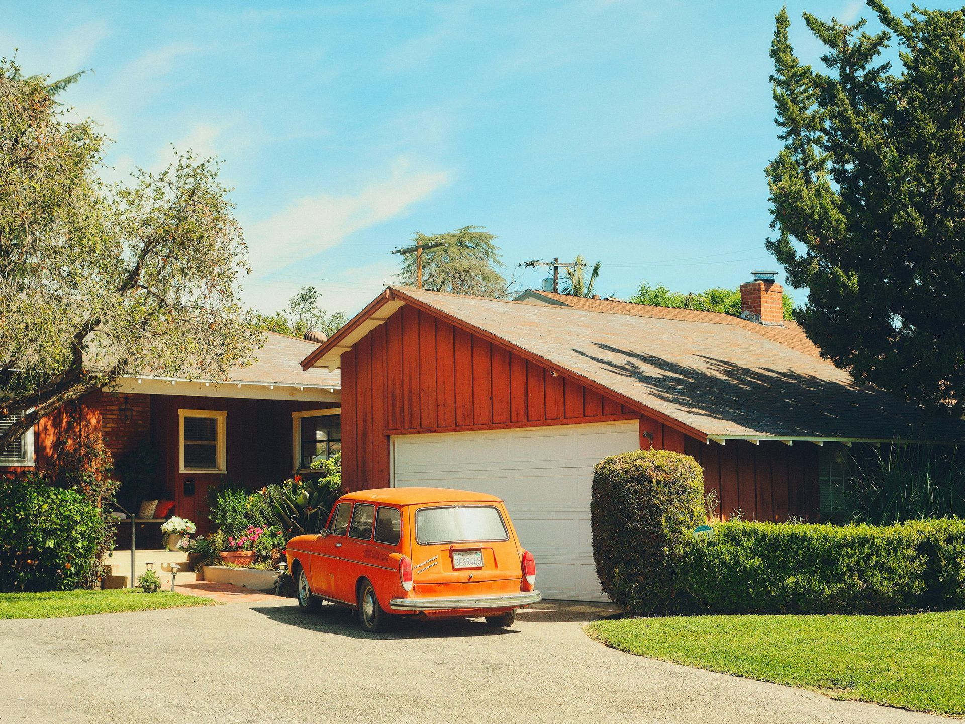 Orange car parked in front of a red house with a white garage and green hedges