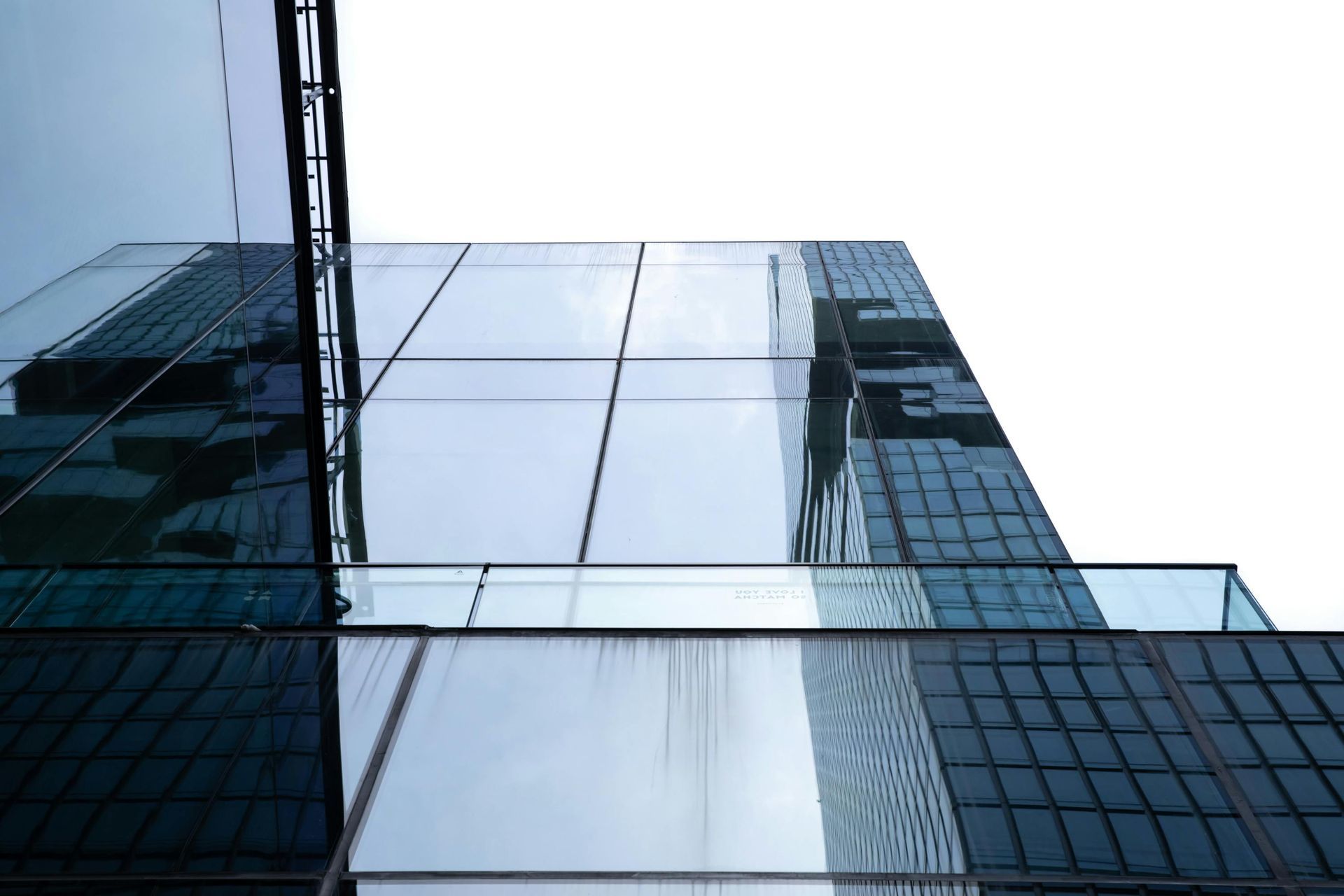 Glass-fronted modern office building seen from below against a cloudy sky
