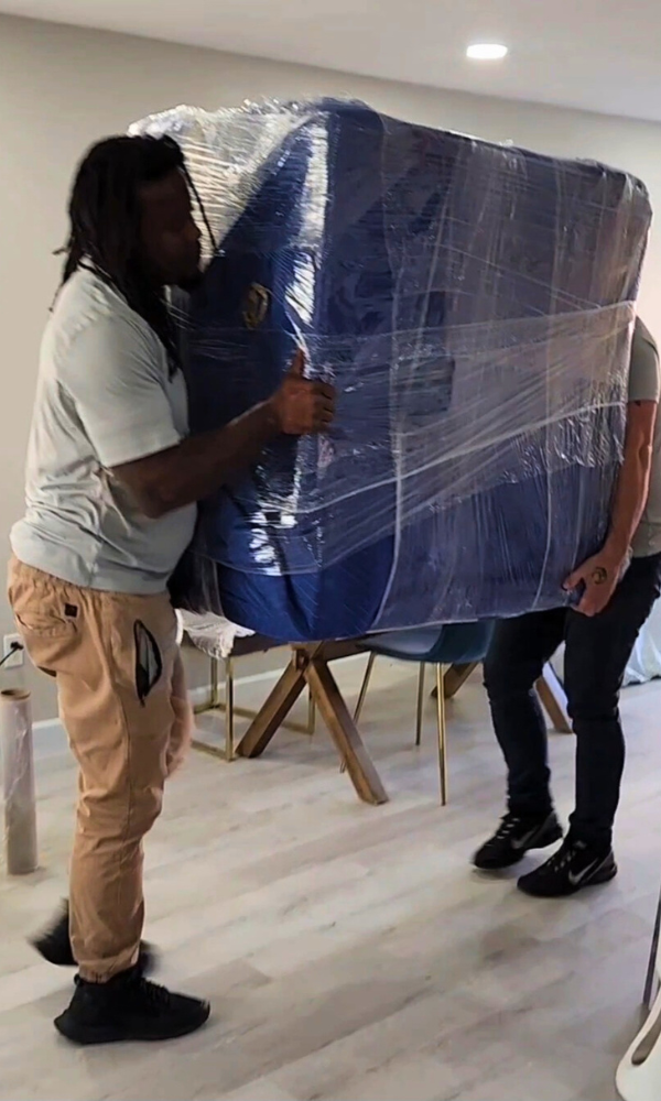 two dallas movers carrying a wrapped sectional 