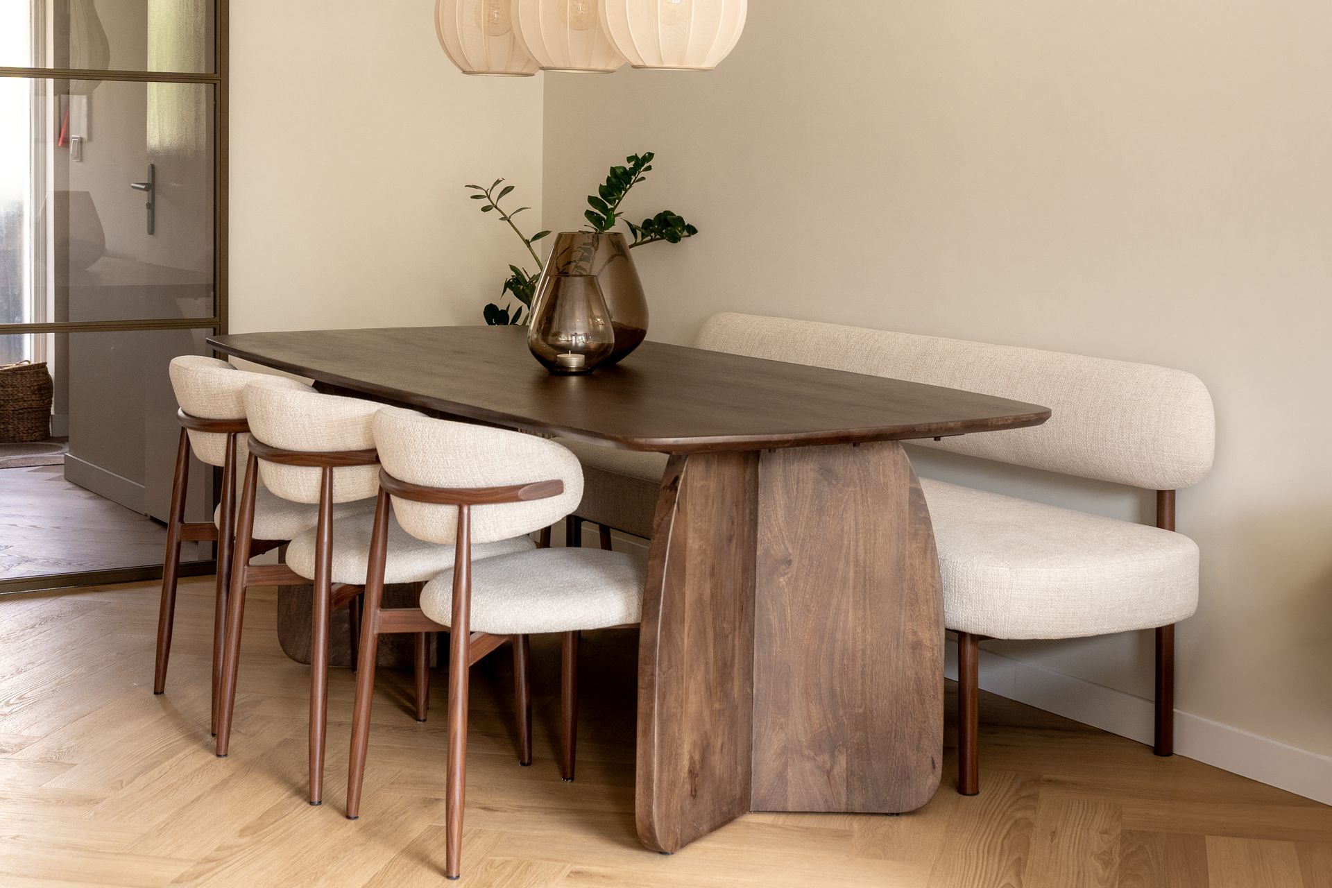 Een moderne eethoek met een donkerhouten tafel, drie crèmekleurige stoelen en een bijpassende bank op een houten vloer.