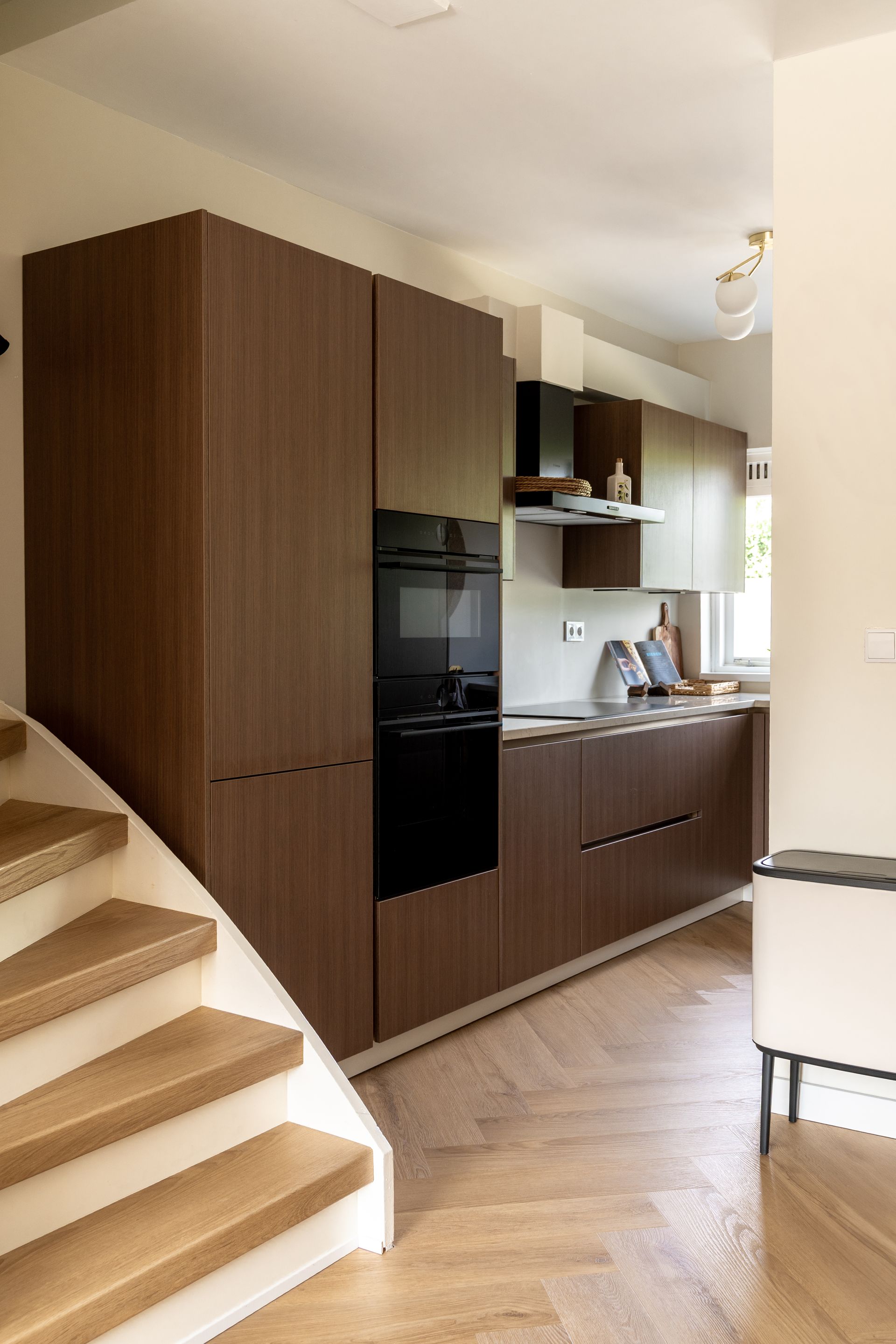 Een moderne keuken met donkerhouten kasten, een ingebouwde oven en een parketvloer, grenzend aan een houten trap.