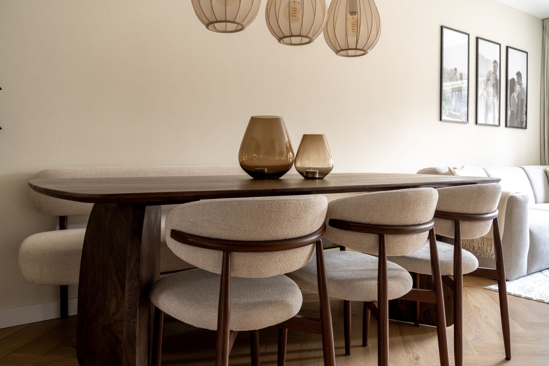 Een moderne eetkamer met een donkerhouten tafel, beige gestoffeerde stoelen, een zitbank en decoratieve glazen vazen.