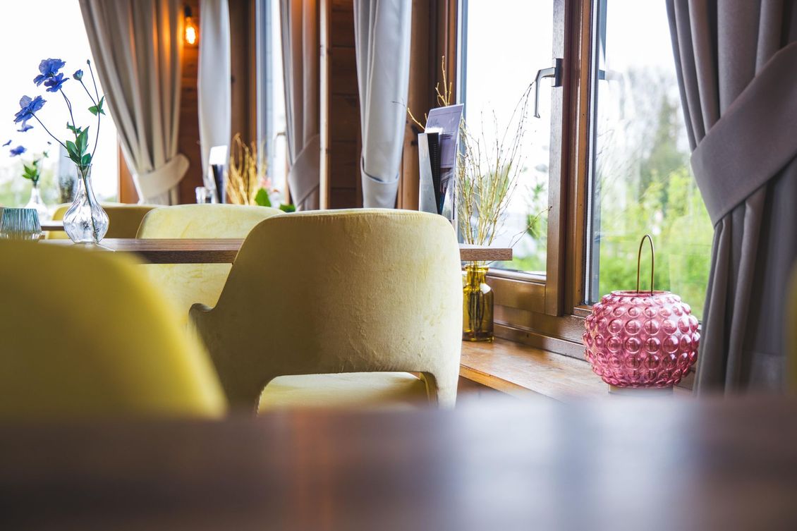 Gele gestoffeerde stoelen staan ​​bij grote ramen met neutrale gordijnen, een roze decoratieve lamp en een vaas met bloemen.