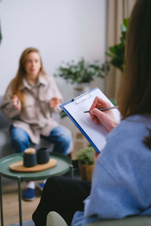 Therapist taking notes as a client talks during a session. Client gestures while seated on couch.