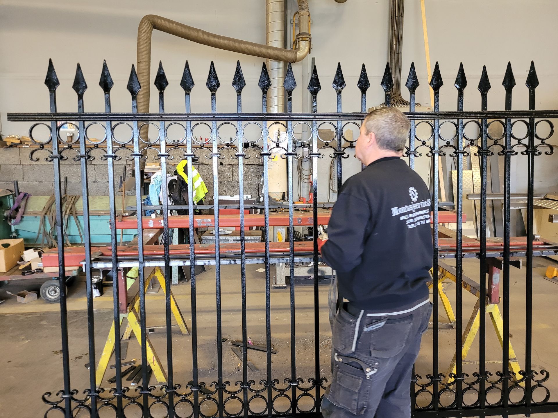 En person arbeider med et svart smijernsgjerde inne i et verksted.