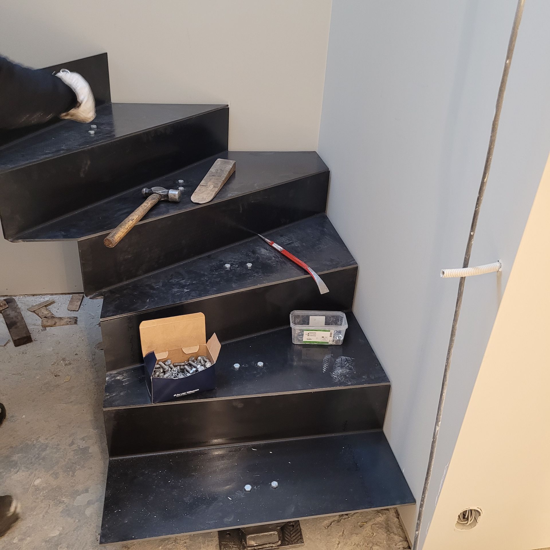 Svart metalltrapp under bygging, med verktøy og festemidler.