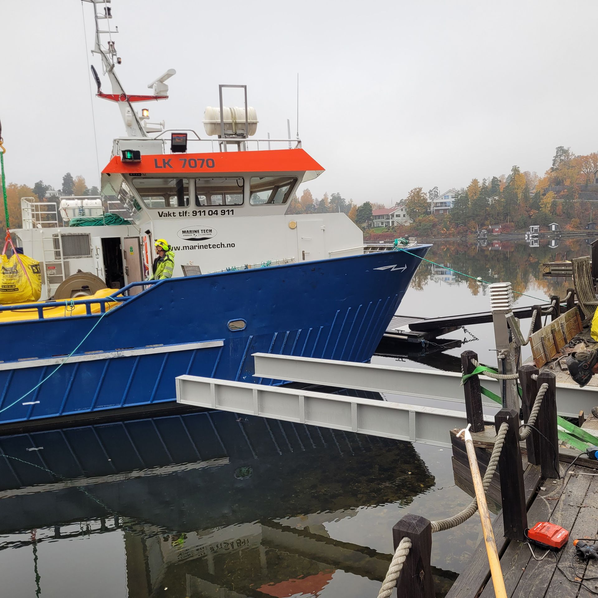 Blå og hvit båt lagt til kai ved en brygge, sannsynligvis et forskningsfartøy, i en rolig havn.