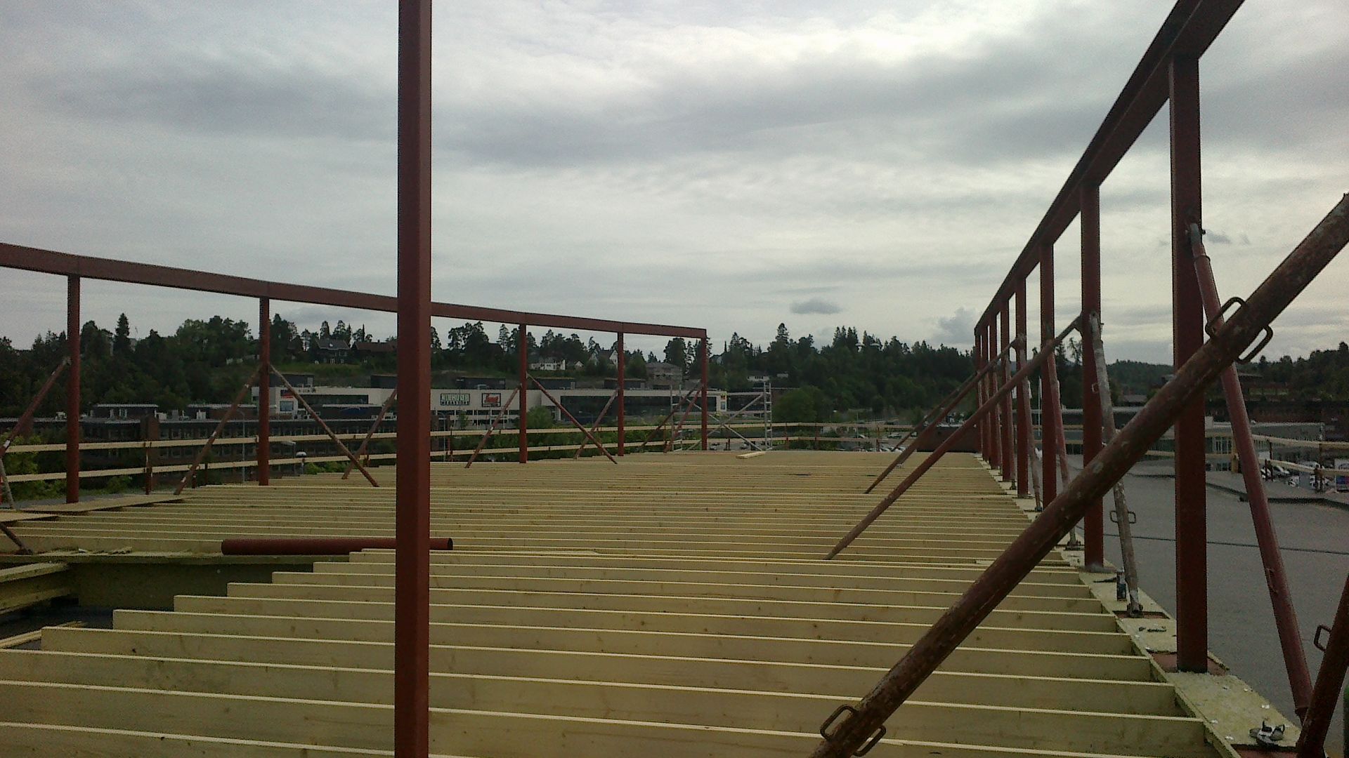 Byggeplass: rødt metallrammeverk på en flat overflate, skog i bakgrunnen, overskyet himmel.