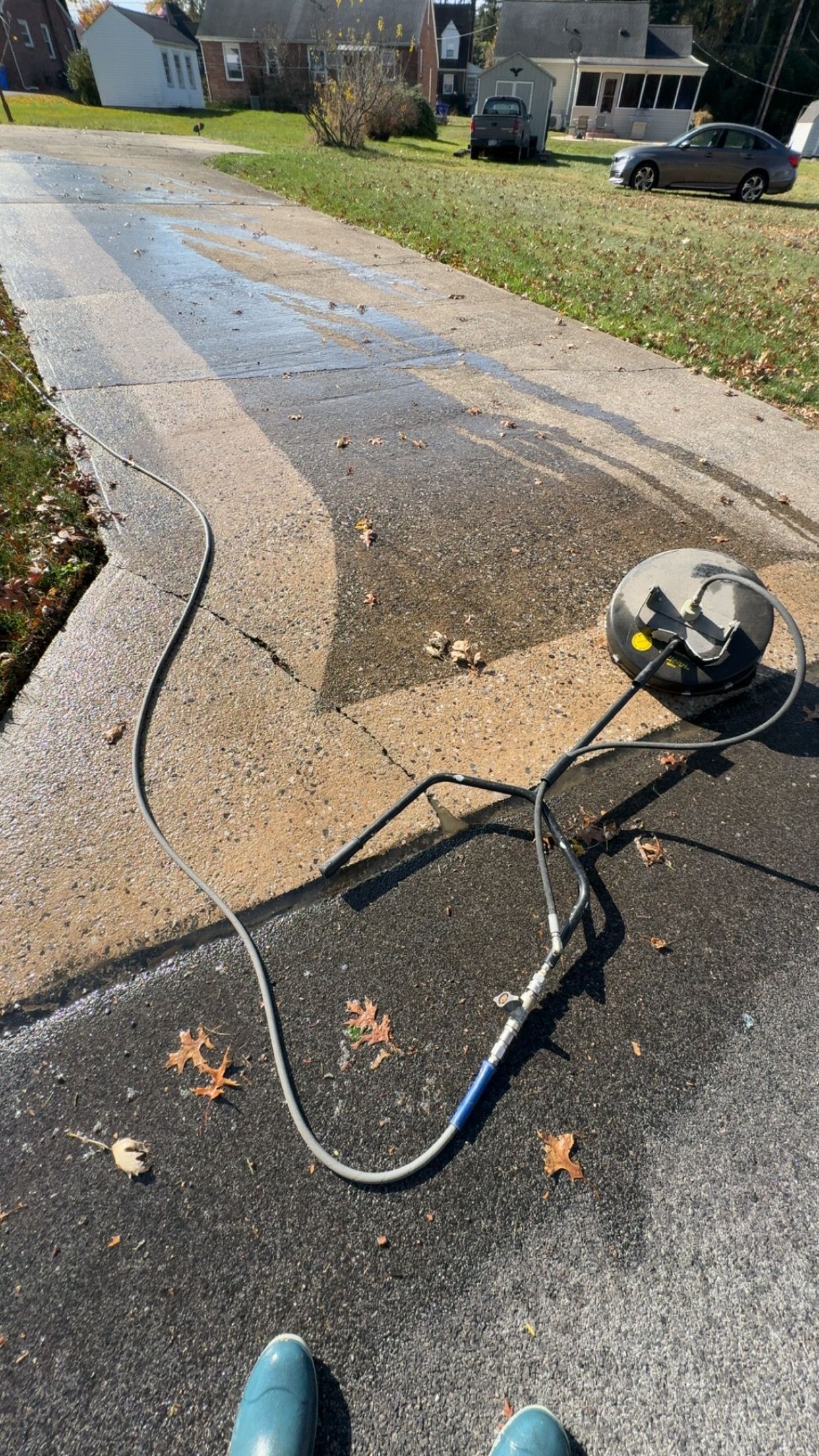 Driveway being pressure washed; half clean, hose and pressure washer visible. Outdoors, sunny.