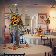 Decorated banquet hall with round tables, autumn centerpieces, and sunflowers in a warm, elegant setting