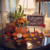 Fall porch display with pumpkins, flowers, autumn leaves, and a “Welcome” sign