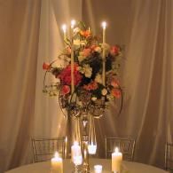 Candlelit floral centerpiece with tall candles on a table in a softly draped room