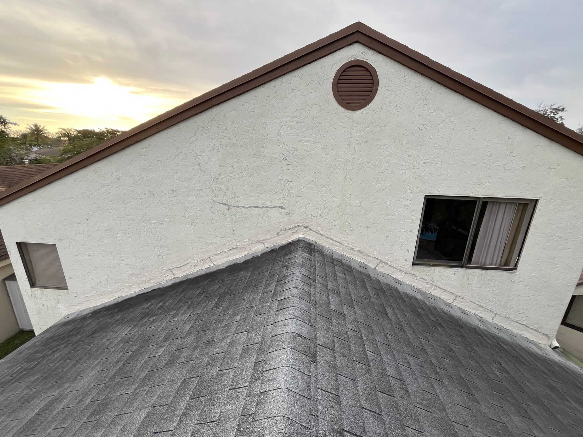 The roof of a white house with a brown roof and a window.