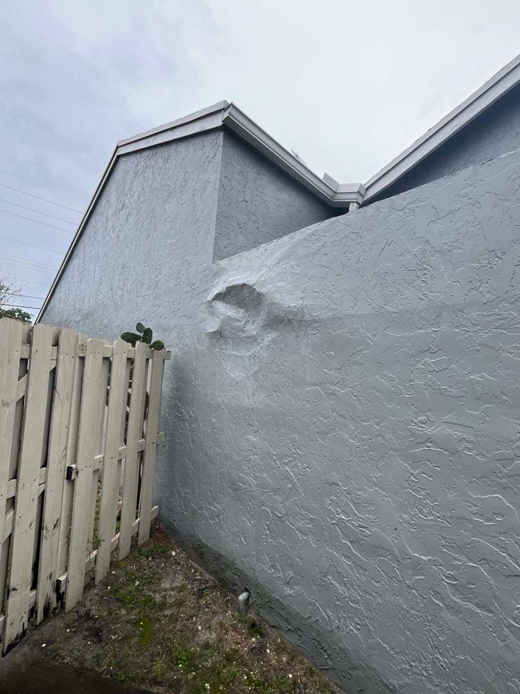 A white fence is next to a gray wall with a hole in it.