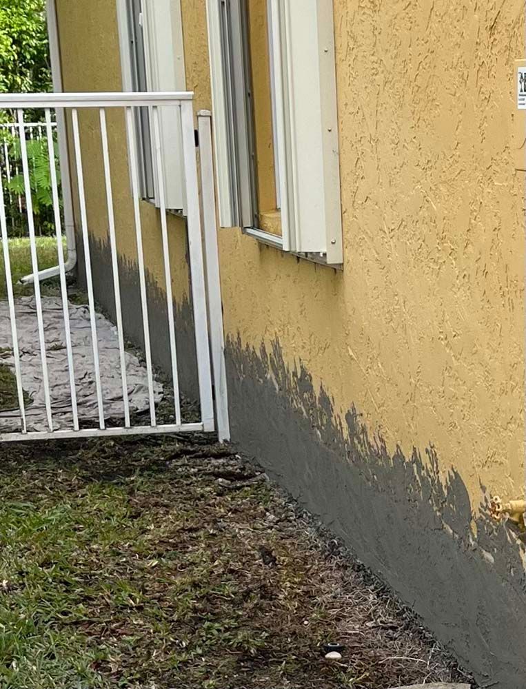 A yellow house with a white railing and a fence in front of it.