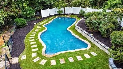 An aerial view of a large swimming pool in a backyard surrounded by grass and trees.