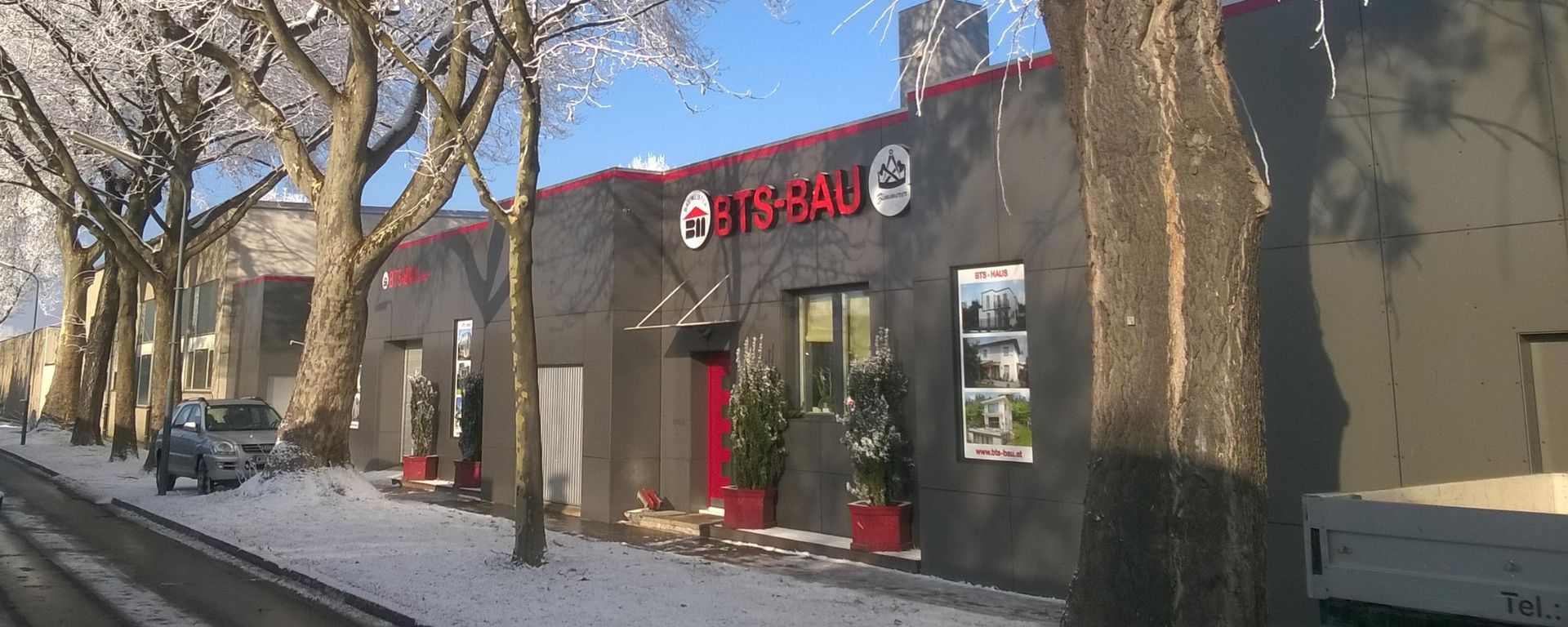Gebäude mit rotem Schild, umgeben von schneebedeckten Bäumen und einer Straße.
