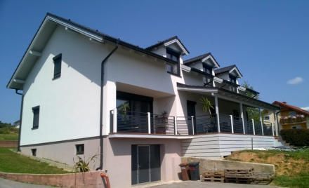 Modernes weißes Haus mit schwarzem Dach und Balkon unter strahlend blauem Himmel.
