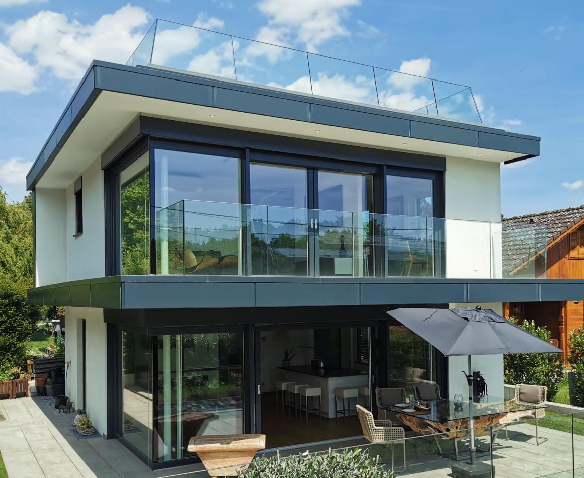 Modernes weißes Haus mit dunkelgrauen Zierelementen, Glasgeländern und einem Essbereich im Freien.