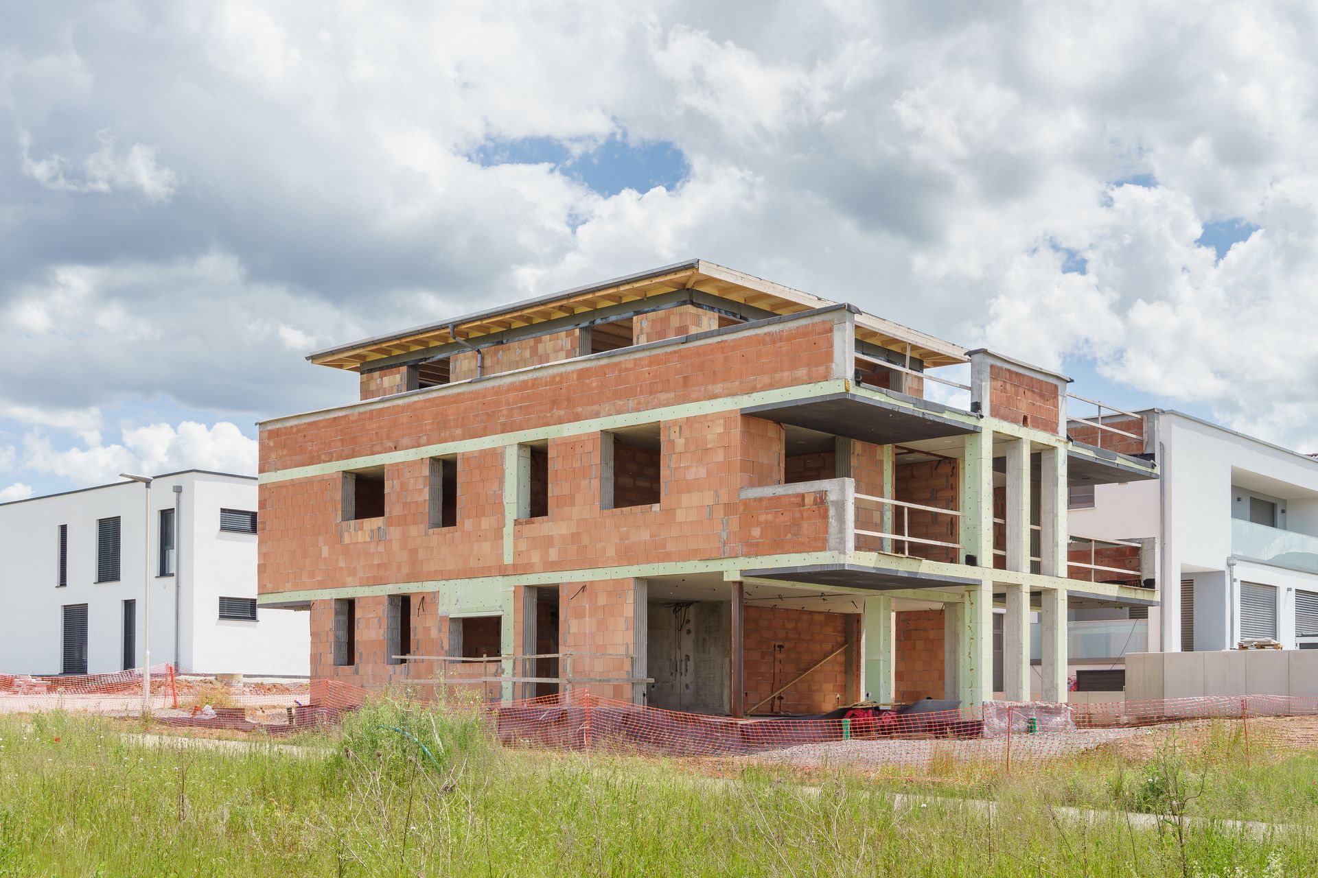 Zweistöckiges Backsteingebäude im Bau, sichtbares Fachwerk, blauer Himmel und grünes Gras.