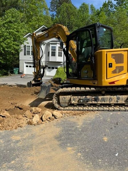 A yellow excavator is moving dirt in front of a house