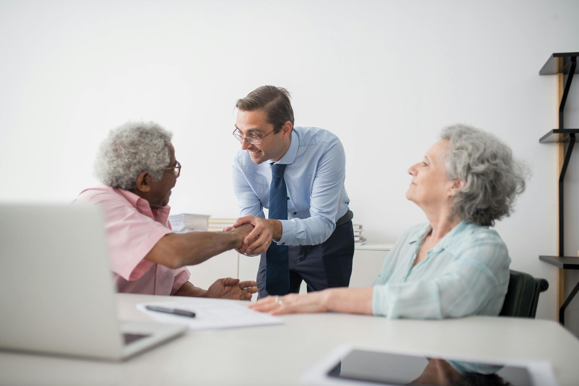 A man is shaking hands with two older women while sitting at a table.