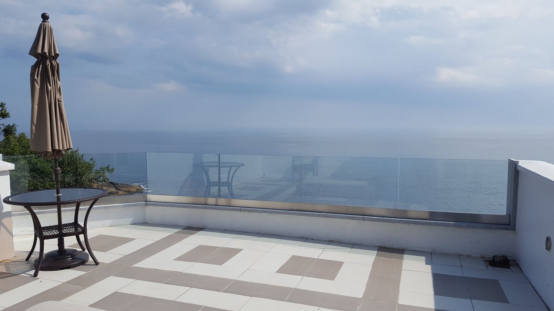 A table and umbrella on a balcony overlooking the ocean.