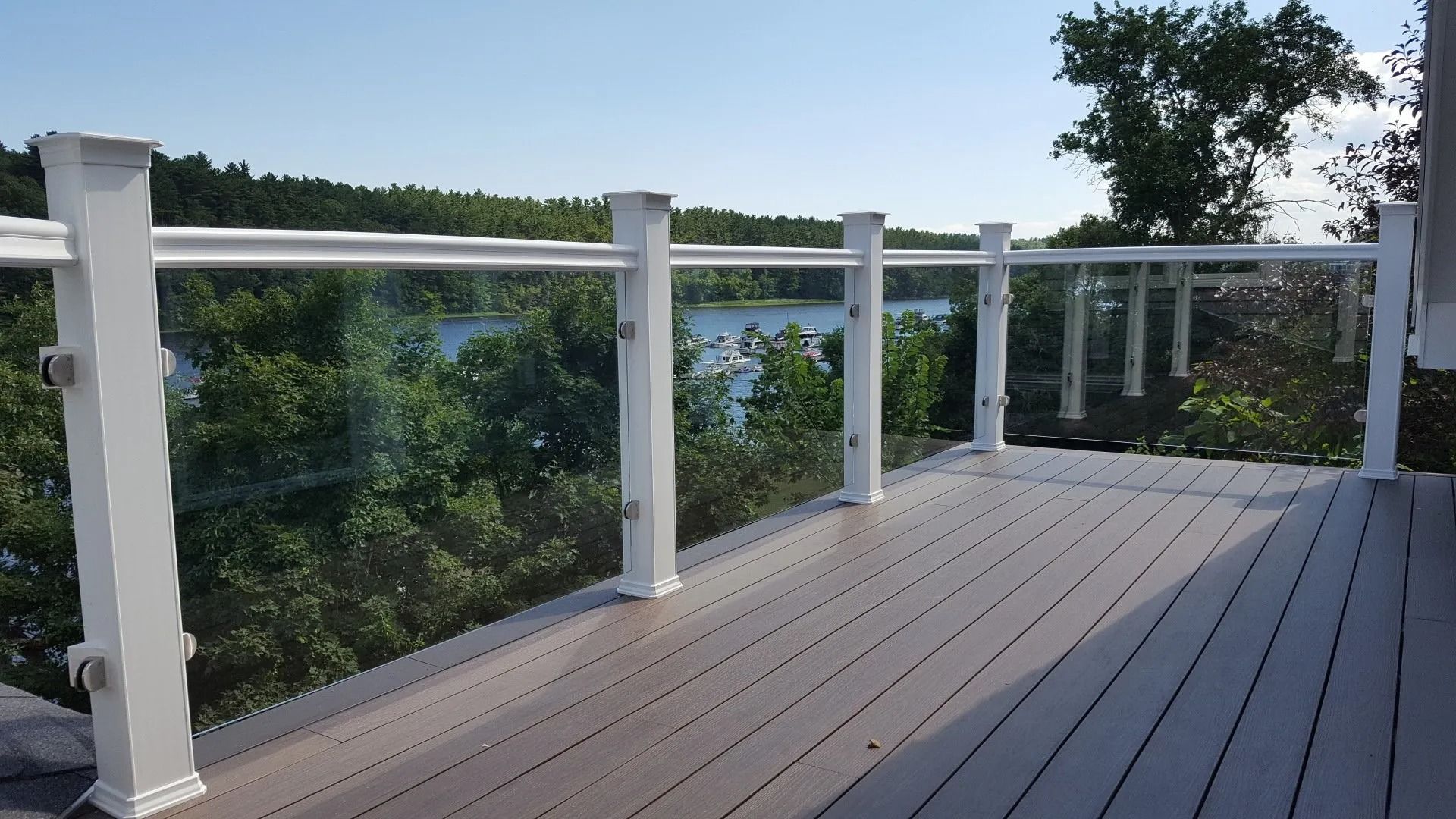 A deck with a glass railing overlooking a lake.
