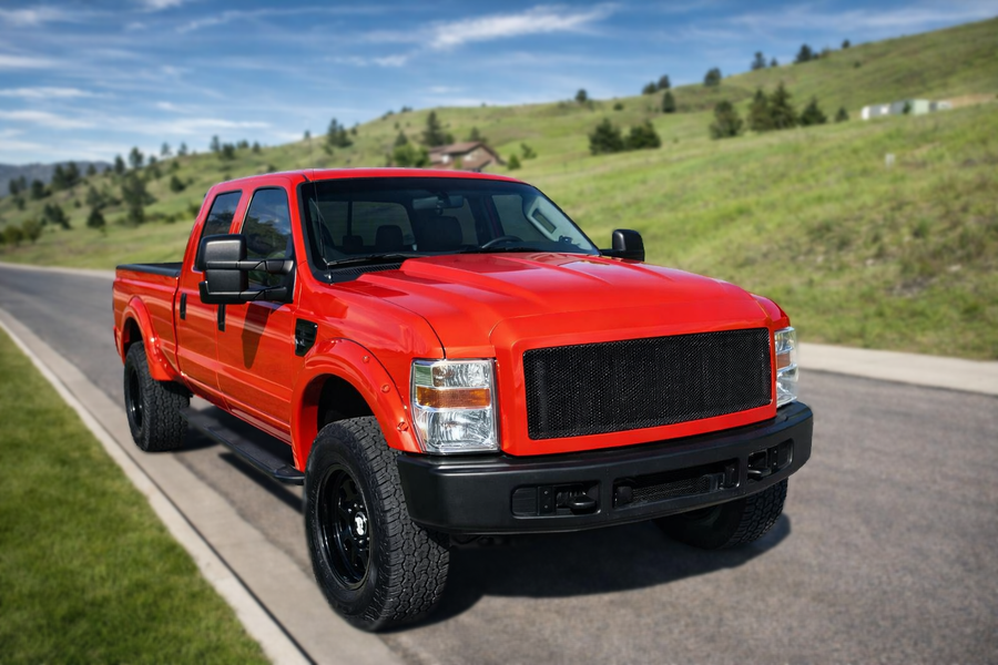 Red pickup truck parked on a paved road, mountains in the background, sunny day.