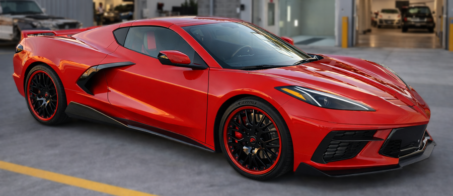 Red Corvette sports car parked on a gray surface in front of an open garage.